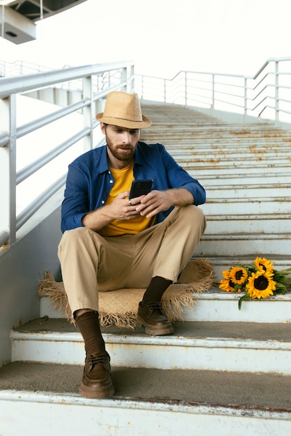 Foto gratuita ritratto di uomo barbuto con smartphone e girasoli sulle scale