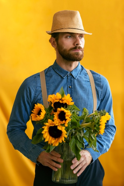 Free photo portrait of bearded man with straw hat and bouquet of sunflowers