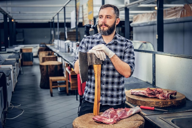 フリースシャツを着たひげを生やした肉の男の肖像画は、斧と新鮮なカット肉を保持しています。