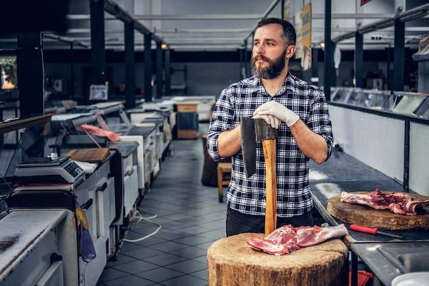 Portrait of a bearded meat man dressed in a fleece shirt holds an axe and fresh cut meat.