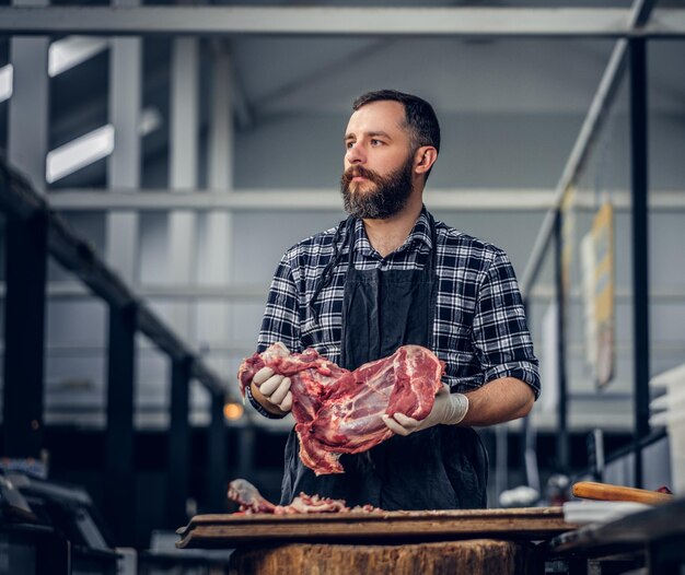 Portrait of a bearded meat man dressed in a fleece shirt holds fresh cut meat in a market.