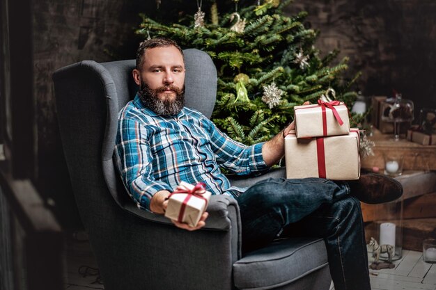 Portrait of bearded middle age male with gift boxes over fir tree in background.