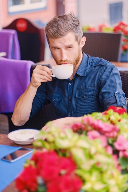あごひげを生やした赤毛のカジュアルな男の肖像画は、通りのカフェでコーヒーを飲みます。