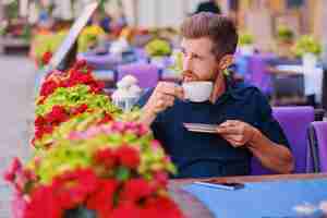 Free photo portrait of bearded redhead casual man drinks coffee in a cafe on a street.