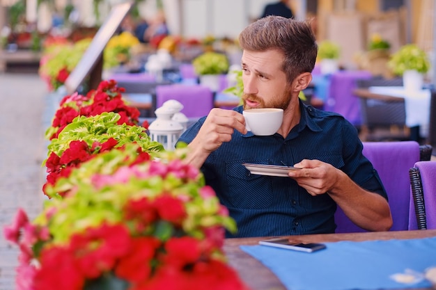 수염난 빨간 머리 캐주얼 남자의 초상화는 거리에 있는 카페에서 커피를 마신다.
