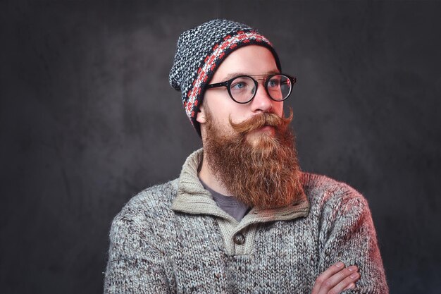ウールのセーターと帽子に身を包んだ眼鏡のひげを生やした赤毛の男性の肖像画。