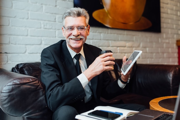 Foto gratuita ritratto di un uomo anziano barbuto che beve caffè in un bar. uomo anziano che utilizza laptop intelligente nella caffetteria.