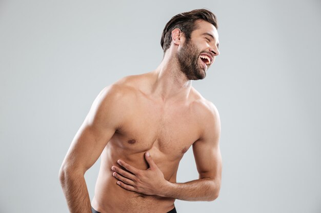 Portrait of a bearded shirtless man doubling up with laughter