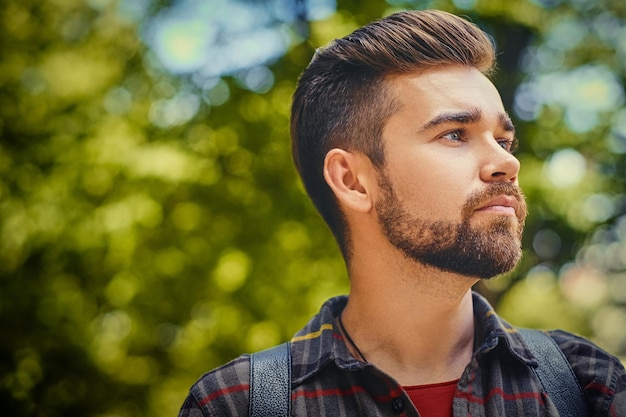 Portrait of bearded traveler male dressed in a fleece shirt over wild park background.