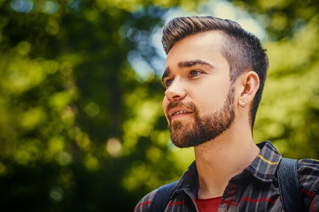 Portrait of bearded traveler male dressed in a fleece shirt over wild park background.