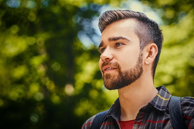 Portrait of bearded traveler male dressed in a fleece shirt over wild park background.