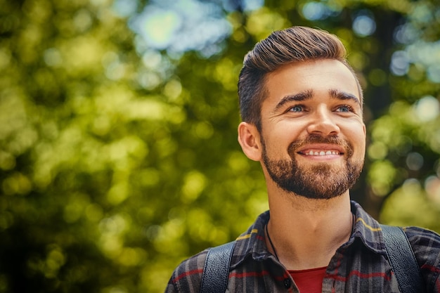 Portrait of bearded traveler male dressed in a fleece shirt over wild park background.