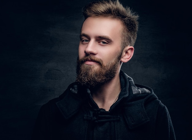 Portrait of a bearded urban male isolated with contrast illumination on grey vignette background.