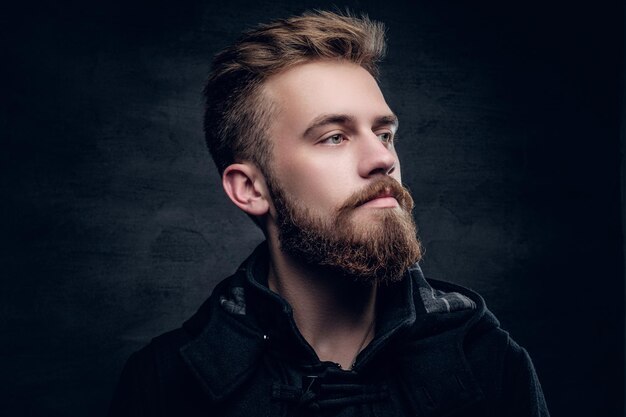 Portrait of a bearded urban male isolated with contrast illumination on grey vignette background.