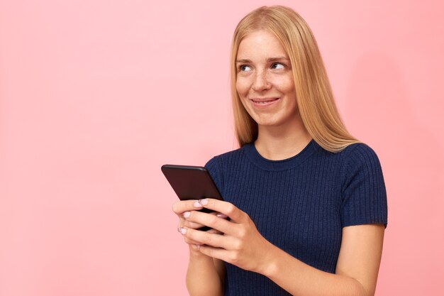 Портрет красивой 20-летней молодой женщины с длинными светлыми волосами, держащей смартфон