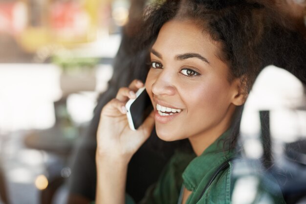 Портрет красивой африканской женщины за стеклом, улыбаясь, разговаривает по телефону