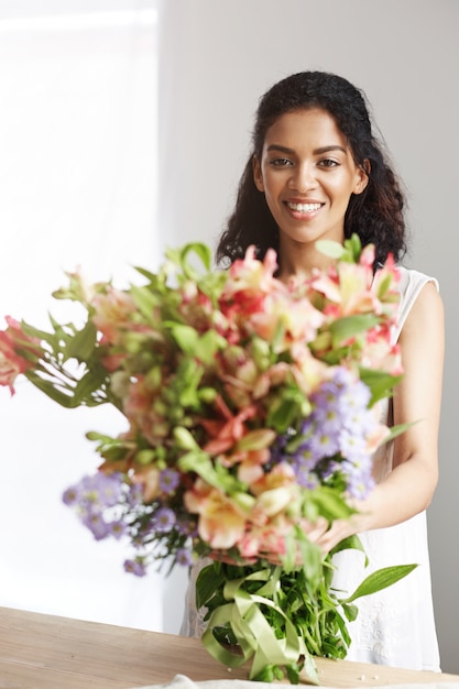 Portrait of beautiful african woman smiling holding bouquet of alstroemerias.