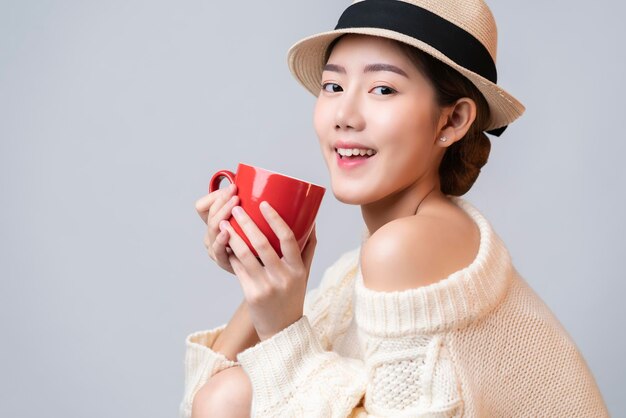 Portrait of beautiful asian female in summer travel dress hand hold red ceramic cup of hot drinh with smile and cheerful white background