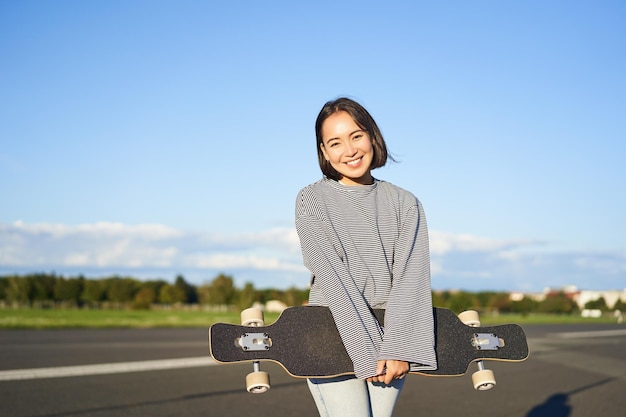 Portrait of beautiful asian girl skating on longboard crusing with skateboard on empty road enjoying