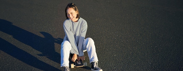 Портрет красивой азиатской девушки катается на коньках сидит на ее скейтборде и улыбается милый подросток с