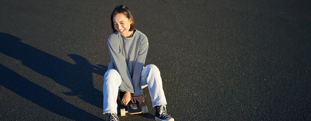 그녀의 스케이트보드에 앉아 아름다운 아시아 소녀 스케이팅의 초상화와 미소 귀여운 십대
