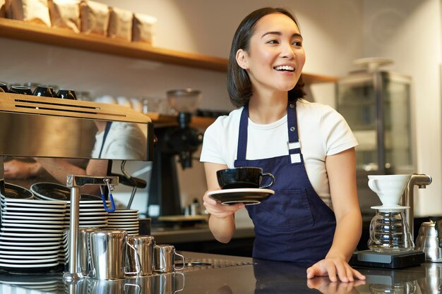 一杯のコーヒーを保持しているカフェでアルバイトをしている美しいアジアの女の子の学生の肖像画は、l を作った