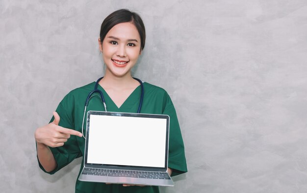 Портрет красивой азиатской женщины-врача, работающей с ноутбуком на сером фоне