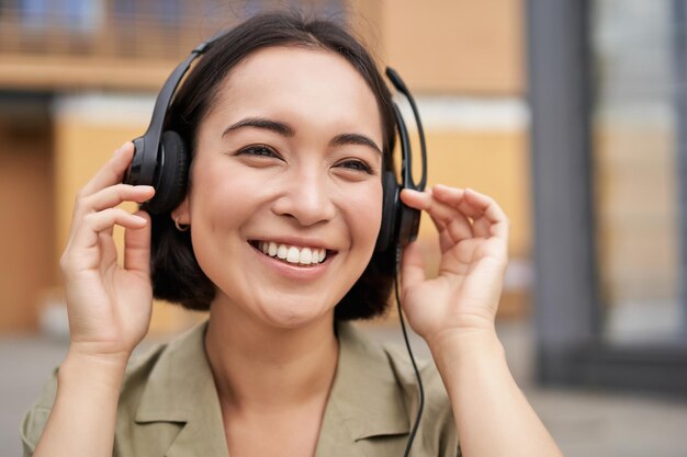 행복 하 게 웃 고 시내 중심가의 거리에서 음악을 듣고 헤드폰에서 아름 다운 아시아 여자의 초상화
