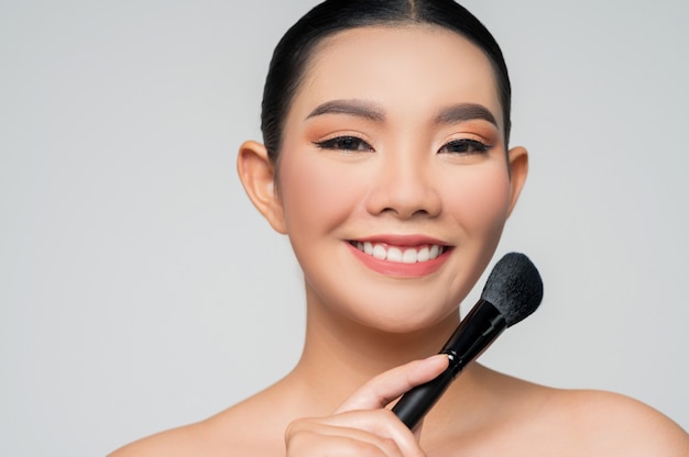 Portrait of Beautiful Asian woman holding makeup blusher brush