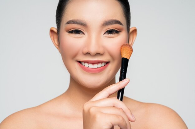 Portrait of Beautiful Asian woman holding makeup blusher brush