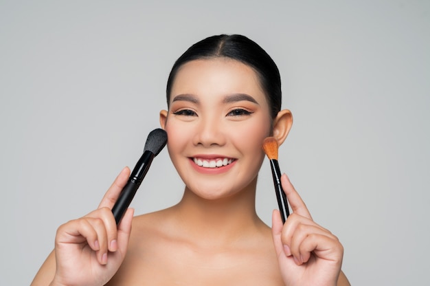 Portrait of Beautiful Asian woman holding makeup blusher brush