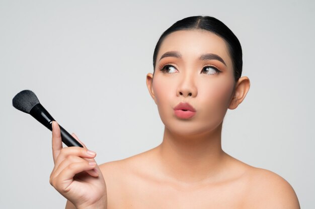 Портрет красивой азиатской женщины, держащей кисть для румян для макияжа