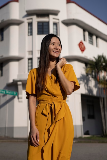 Free photo portrait of beautiful asian woman posing in the city while wearing yellow dress