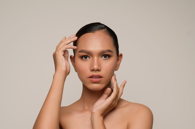 Портрет красивой азиатской женщины касается щеки и лба, красивой естественной чистой кожи