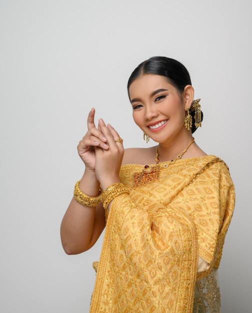Портрет красивой азиатской женщины в традиционном тайском платье, костюм улыбается и изящно позирует на белой стене