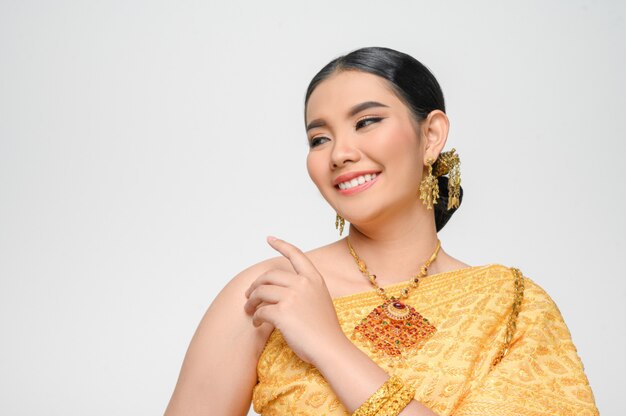 Портрет красивой азиатской женщины в традиционном тайском платье, костюм улыбается и позирует рука на плече с изящно на белой стене