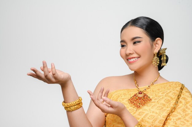 Portrait Beautiful Asian woman in traditional Thai dress costume smile and pose open palm with gracefully on white wall