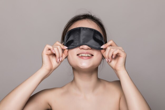 Portrait of beautiful asian woman wearing a sleeping mask isolated on gray wall