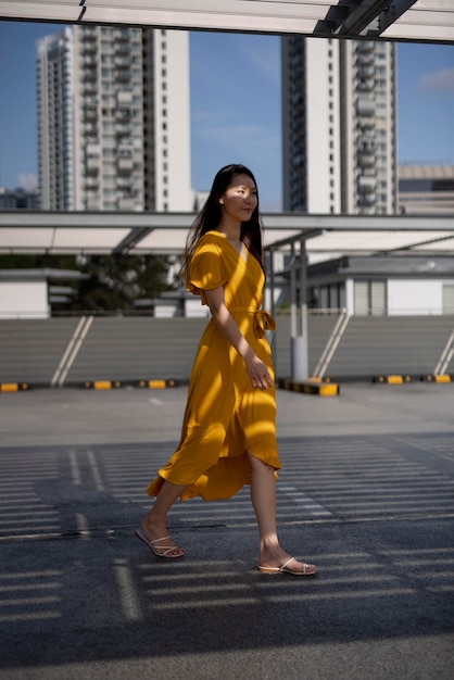 Foto gratuita ritratto di bella donna asiatica in vestito giallo che posa all'aperto nella città