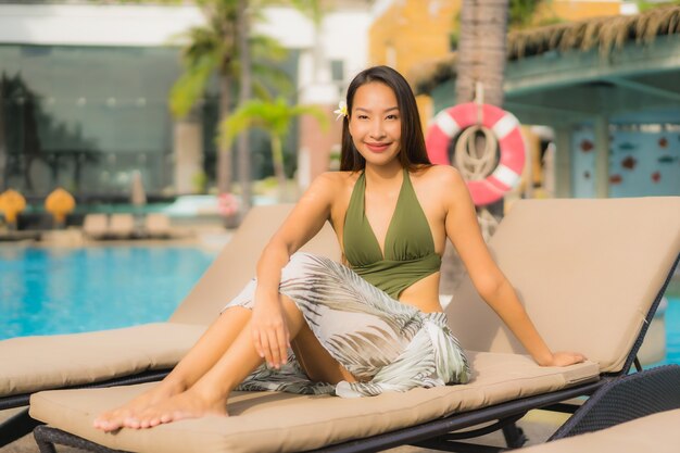 Улыбка красивых азиатских женщин портрета счастливая ослабляет вокруг бассейна в курорте гостиницы