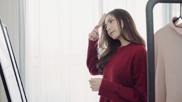 Portrait of beautiful attractive Asian woman combing her hair and choosing clothes in her dressing room at home.