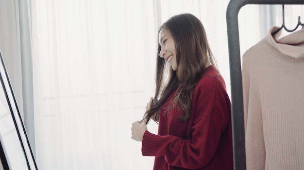 Portrait of beautiful attractive Asian woman combing her hair and choosing clothes in her dressing room at home.