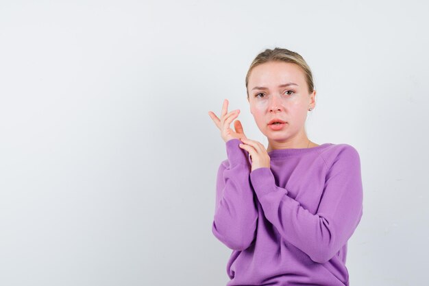 Portrait of beautiful attractive blonde girl in purple sweater making beauty gesture isolated on white background