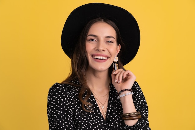 Portrait of beautiful attractive woman posing isolated on yellow background wearing black dotted dress and black hat