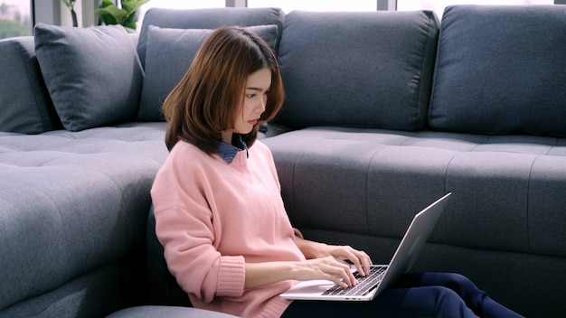 Portrait of beautiful attractive young smiling Asian woman using computer or laptop while lying on the sofa 