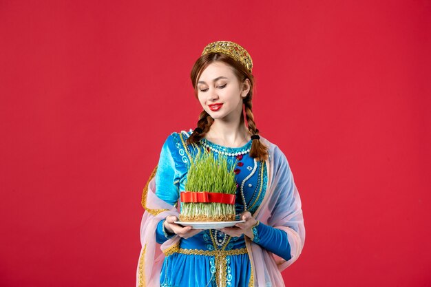 Portrait of beautiful azeri woman in traditional dress holding semeni on red