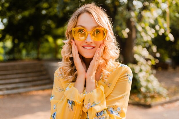 Portrait of beautiful blond stylish emotional woman in yellow blouse wearing sunglasses, funny crazy face expression