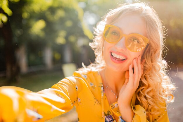 셀카를 만드는 선글라스를 착용하는 노란색 블라우스에 아름다운 금발 세련된 웃는 여자의 초상화 photo