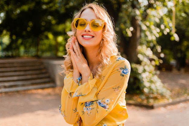 Портрет красивой блондинки стильной улыбающейся женщины в желтой блузке в солнцезащитных очках
