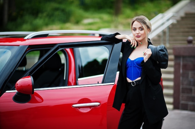 Free photo portrait of beautiful blonde sexy fashion woman model in cap and in all black blue corset with bright makeup near red city car